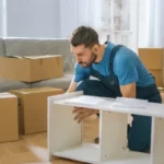 professional mover assembling shelving unit with moving boxes in the background.