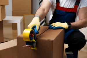 Professional mover crouched down, taping a moving box with additional boxes in the background