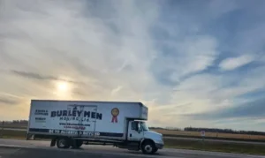 2 Burley Men Moving truck parked on the side of the highway with the sun shining through clouds in the background.