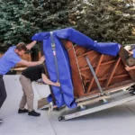 Three movers loading a grand piano up the ramp into the back of a moving truck.