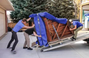 Three movers loading a grand piano up the ramp into the back of a moving truck.